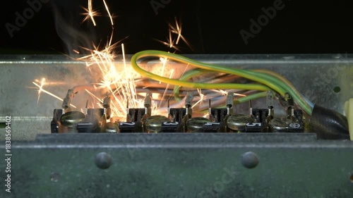 An open electrical panel demonstrates a short circuit with intense sparks and smoke.