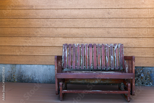 Welcoming relaxing rustic textured primitive old weathered wooden country bench against wood panel background backdrop on a porch for advertising or greeting card