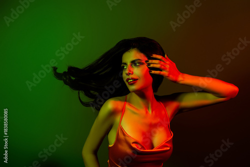 Stylish woman in a satin dress highlighted by vibrant green and red neon lights, exuding elegance and passion