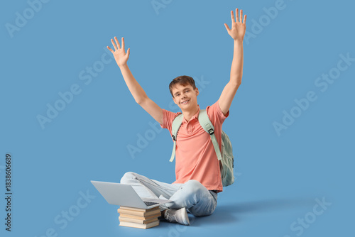 Male student with laptop and books studying computer sciences on blue background