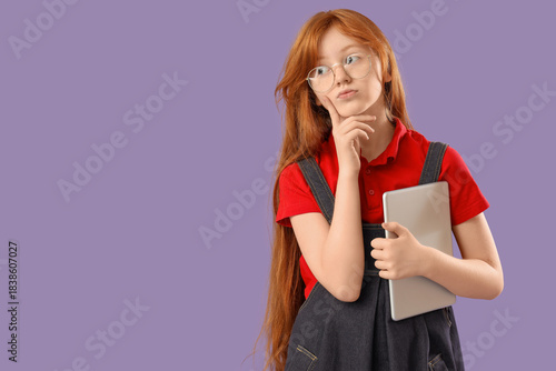Thoughtful schoolgirl with modern tablet computer on lilac background