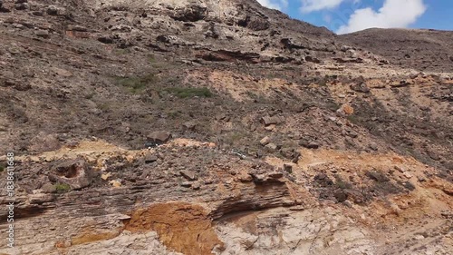 Aerial view of driving cars in dry valley in the island of Socotra. Motion drone video of moving cars on bumpy road surrounded by stones and dessert plants. Following cars from the air. Off-road drive