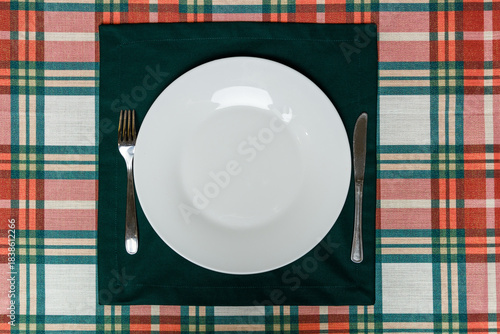 White plate and cutlery on green placemat over plaid tablecloth