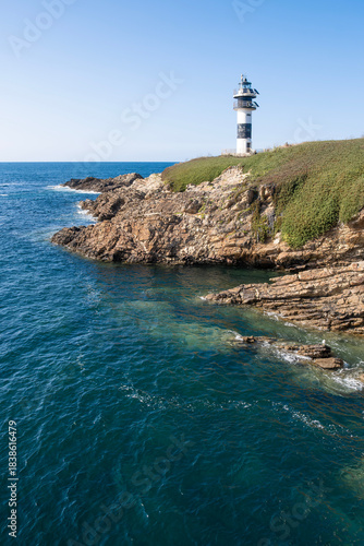 Modern black and white lighthouse standing on a rocky cliff by the deep blue sea under a clear sky, Isla de Pancha, Ribadeo, Galicia, Spain