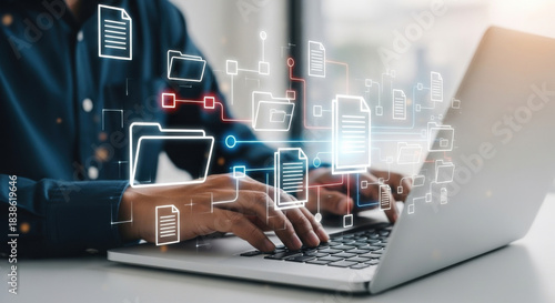 Close up of a man typing on silver laptop with digital file icons, symbolising the data being transferred, displayed on a white tabletop under soft lighting.