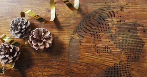 Clustering three frosted pine cones with metallic gold ribbon on warm wooden tabletop, dotted globe