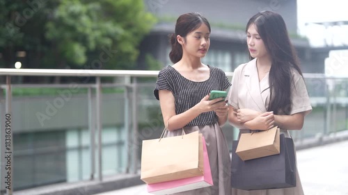 Two asian woman shopping outdoors using credit card and smartphone for mobile payment, concept of cashless society, online transaction, e-commerce, modern lifestyle and digital financial technology