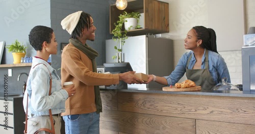 Diverse couple entering cafe ordering pastries to-go, getting box while barista adjusting dome