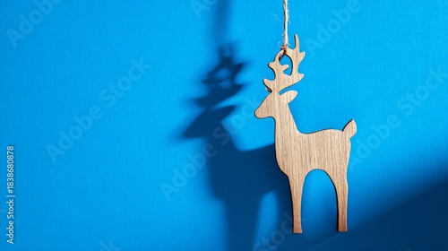 A vertical shot of a deer-shaped wooden Christmas ornament isolated on a blue...