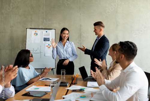 Quadro em tela In an office boardroom, a diverse team greets a new Asian female colleague with smiles and applause