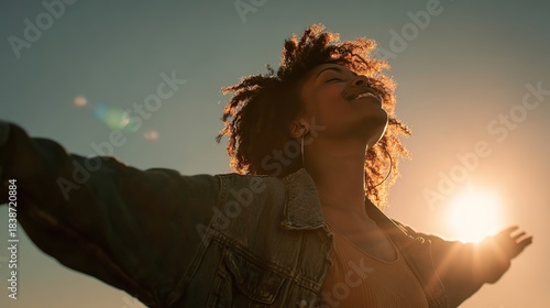 A joyful Black woman with curly hair, embracing the golden sunset with arms open wide, her silhouette backlit by sunlight flares, evoking the freedom and joy of Africa's Day of Freedom.