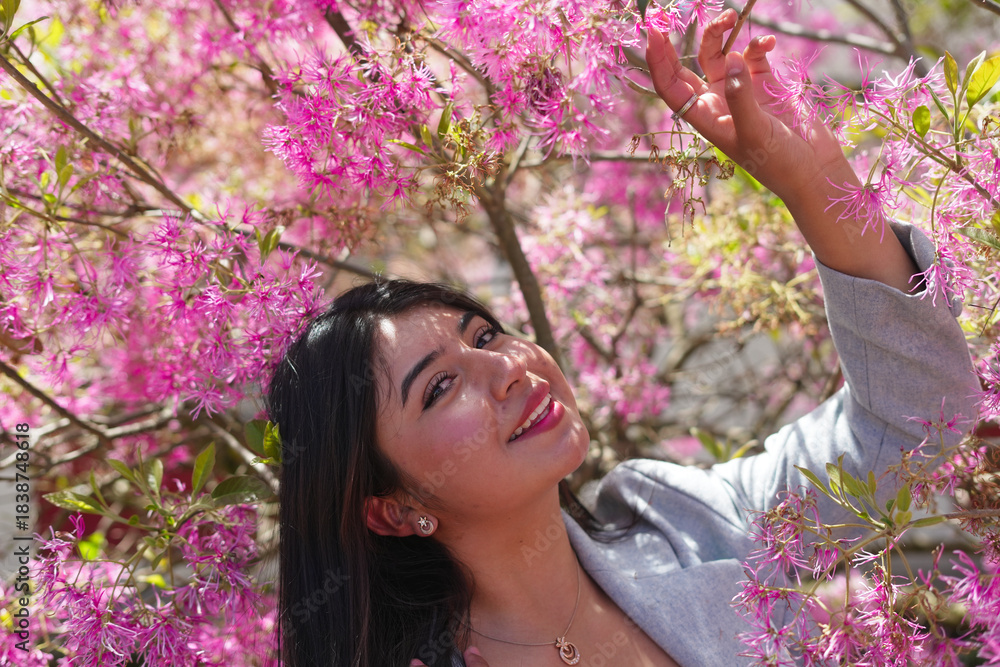Fototapeta premium Young woman smiling among vibrant pink spring flowers