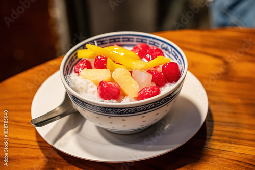 A bowl of Thai Red Ruby dessert or Tub Tim Krob with jackfruit and ice in coconut milk on a wooden table.