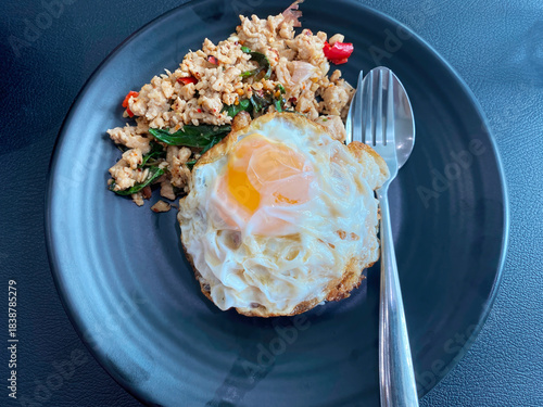A classic Thai dish of spicy basil minced pork stir-fry served over rice with a crispy fried egg on a black plate.
