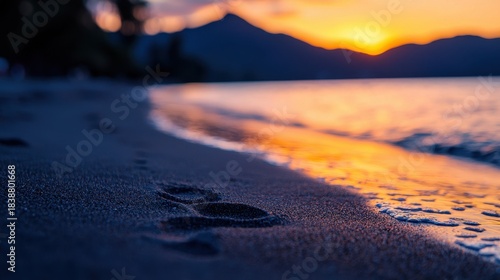 Tranquil Beach Landscape with Footprints at Sunset Over Serene Waters and Mountains
