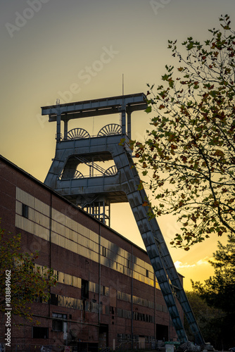 Die Stahlkonstruktion des Fördergerüsts ragt als kühne Silhouette in den warmen, schwelgenden Glanz der Abenddämmerung. Es ist ein geometrisches Meisterwerk, ein stummer Wächter über das lange, massiv