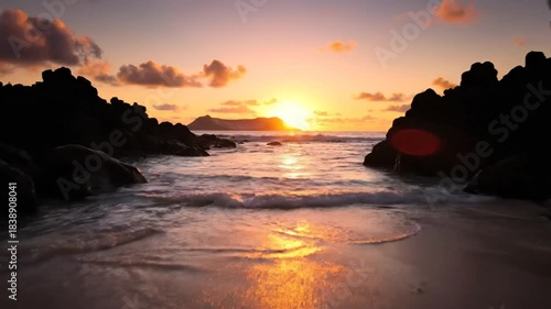 Tranquil beach at sunrise with golden light reflecting in calm ocean water and silhouetted rocks