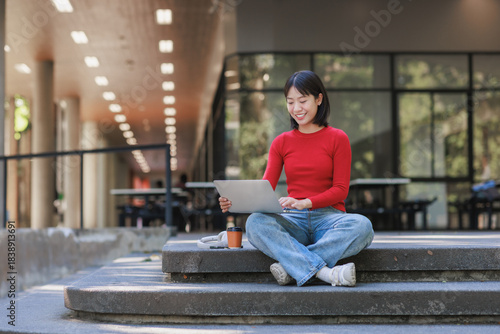 Young student working on laptop on campus steps