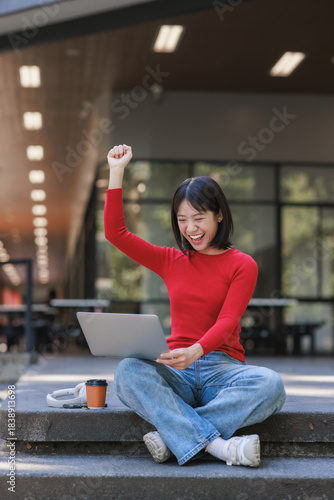 Young woman celebrating success looking at laptop