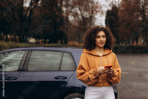 Young woman standing by car using smartphone outdoors