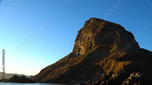 Coastal mountain rising from the ocean waters with beautiful blue sky on a bright sunny day