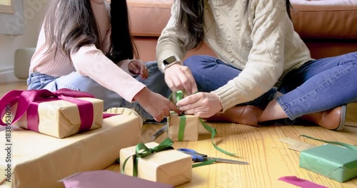 Mother and daughter picking green ribbon and tying bows on gift boxes for Christmas at home