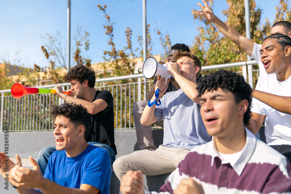 Fototapeta premium Diverse group of male fans watching a sport event from the stadium stands, celebrating and making noise together