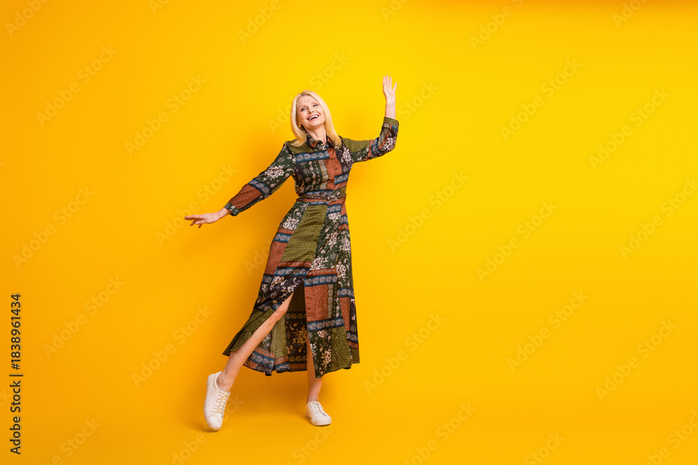 Obraz premium Glamorous mature woman in patchwork dress dances joyfully against a bright yellow background