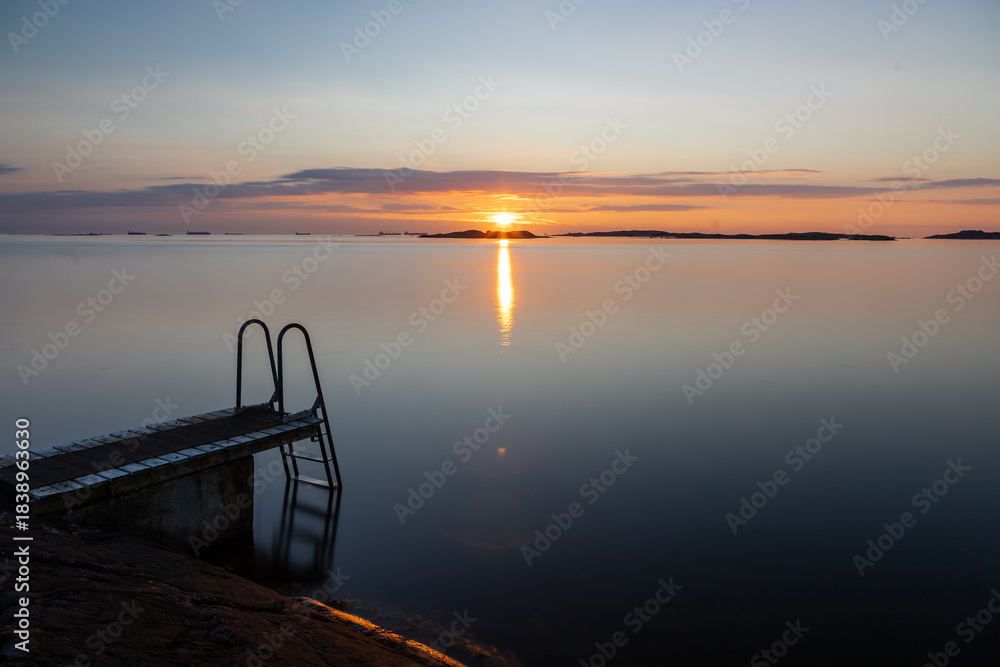 Fototapeta premium Beautiful summer evening with a spectacular sunset over the Gothenburg Archipelago and the calm water of the North Sea seen from the rocky coastline of the small island Vrango with a swimming jetty