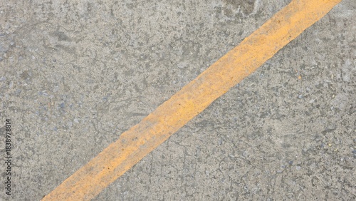 Fototapeta Naklejka Na Ścianę i Meble -  Close-up of a rough concrete surface texture with small aggregates, featuring a faded diagonal yellow line on a driveway or road.