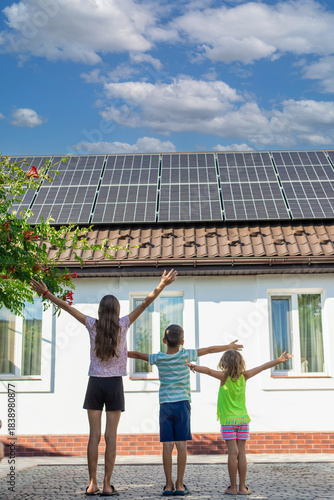 Three children with open arms standing in front of a house with solar panels