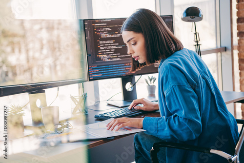 Vászonkép Female programmer works in a bright office coding at a dual monitor setup while