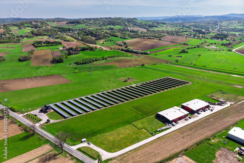 Renewable energy source. Aerial panorama of a massive solar PV power plant installation surrounded by lush green fields in a rural setting, symbolizing technology and sustainability.