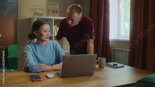 Boss man checks asian woman subordinate do task correctly report. Management satisfied work. Employee right answer. Good job. Guy show laptop screen. Multi racial national couple online shopping home.