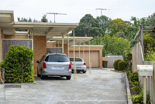 Suburban townhouse driveway with covered carports and parked vehicles beside brick residential units in Australia. Concept of parking, shared access driveway, and private vehicle storage
