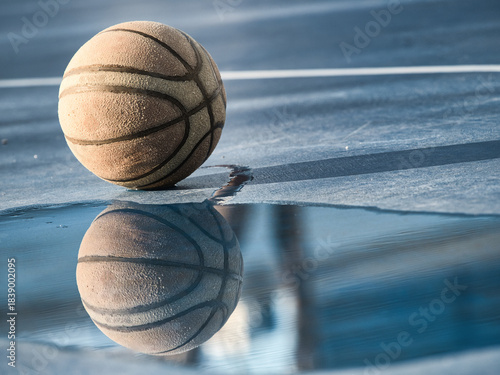 Old basketball on the court has standing water.