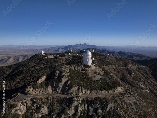 Aerial view of the stark white domes of Kitt Peak Observatory gleam under a vast blue sky, nestled amidst the rugged, sun-drenched mountains, Tucson, Arizona, United States.