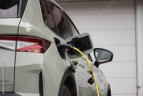 An electric vehicle is connecting to a charging station in a residential area during daylight hours.