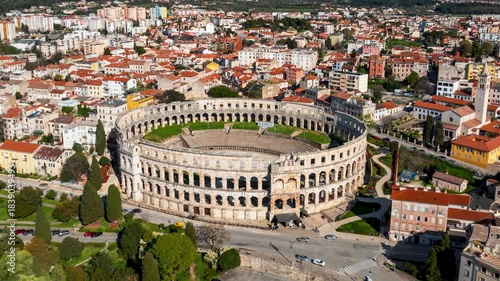 Aerial view of the Pula Arena, a grand Roman amphitheater, standing majestically amidst the city's red-roofed buildings and lush greenery, Pula, Istarska zupanija, Croatia.