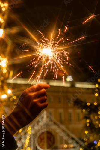 hand holding sparkler in front of Christmas tree. picture shows festive and joyful mood, as it reflects the excitement of the festive season. New Year's Eve and Christmas celebrations. holidays.