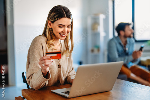 Smiling woman holding a credit card and shopping online at home with a laptop, online purchase