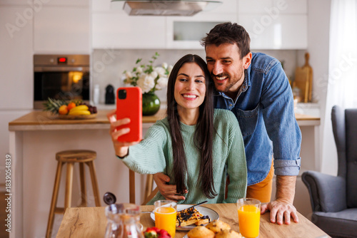 Couple taking selfies using smart phone while having breakfast at home