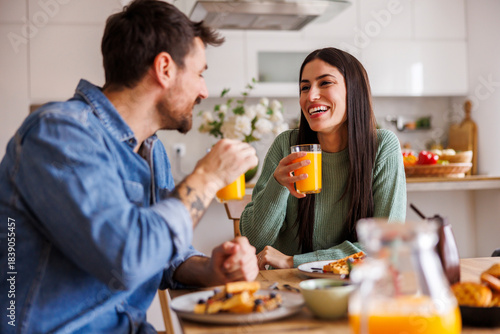 Couple drinking fresh orange juice while having breakfast at home
