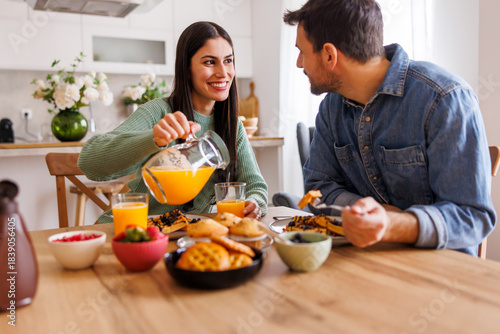 Couple pouring fresh orange juice while having breakfast at home