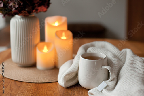 Cozy winter home interior with warm candlelight, wool sweater, hot tea and LED decor creating a calm hygge atmosphere