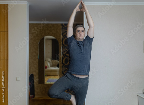 Plus-size man practicing yoga at home on a mat, stretching to improve flexibility, joint mobility and posture. Concept of home fitness, rehabilitation, wellness and mindful movement.