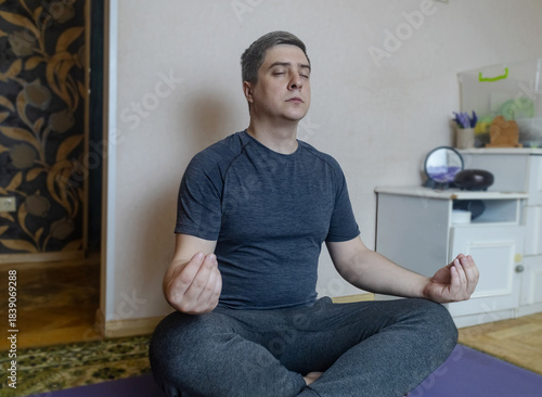 Plus-size man practicing yoga at home on a mat, stretching to improve flexibility, joint mobility and posture. Concept of home fitness, rehabilitation, wellness and mindful movement.