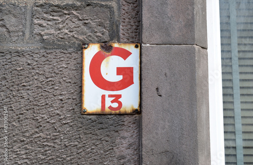 Close up of Worn Enamelled Metal Sign 'G13' Beside Window on Old Stone Building  