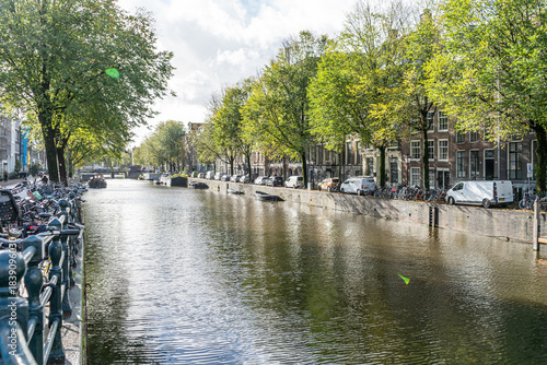 Amsterdam water canal. Architecture and transportation along embankment. Houses and streets. Green trees