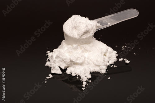 Fotografie A scoop of creatine monohydrate powder on a black reflecting surface